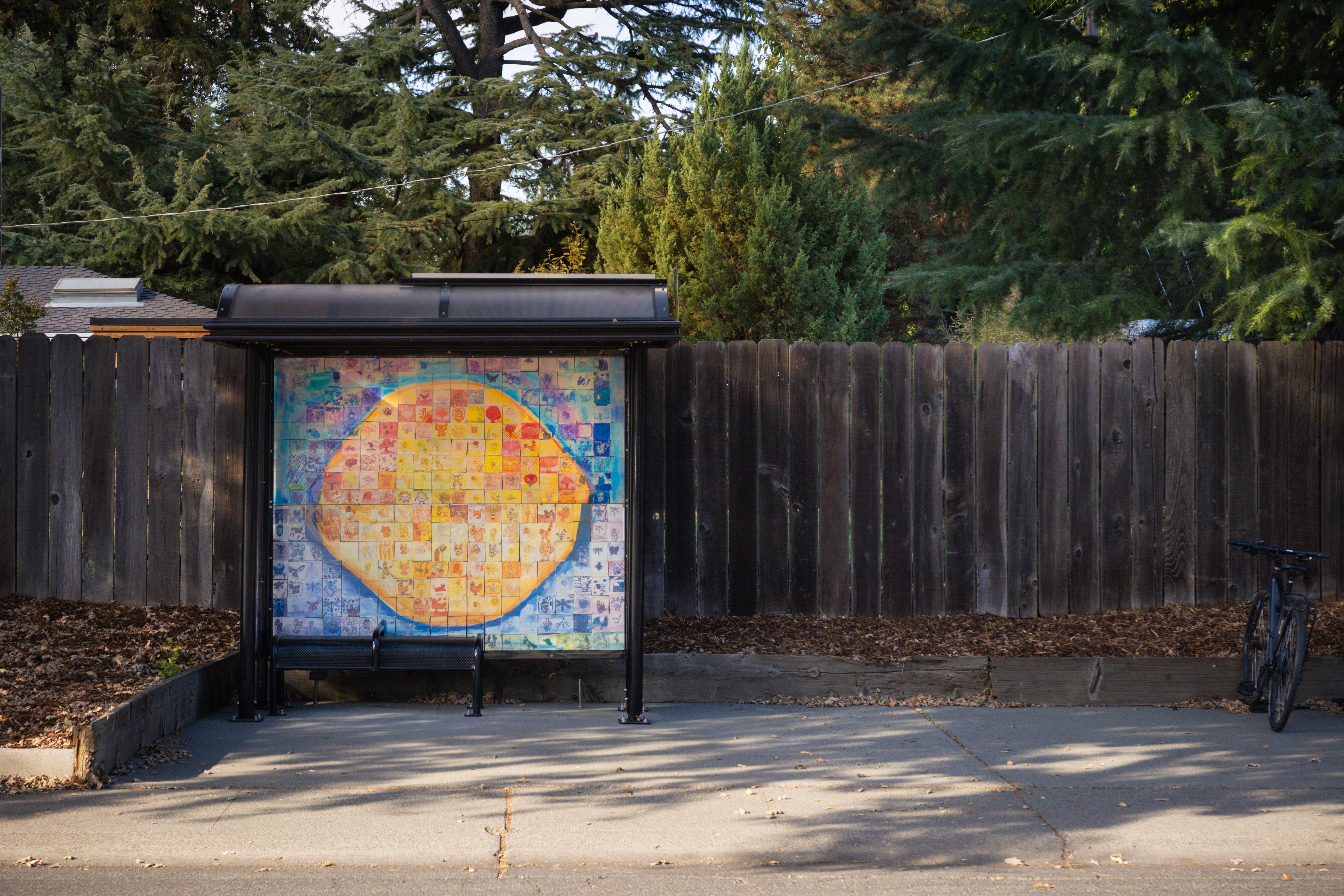 Bus shelter displaying a colorful circular map mural, wooden fence and parked bike.Bus shelter on Loyola Drive at Whittier featuring an art installation by the students of Birch Lane Elementary School.